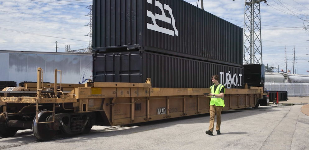 Intramotev TugVolt railcar carrying shipping containers alongside an operator